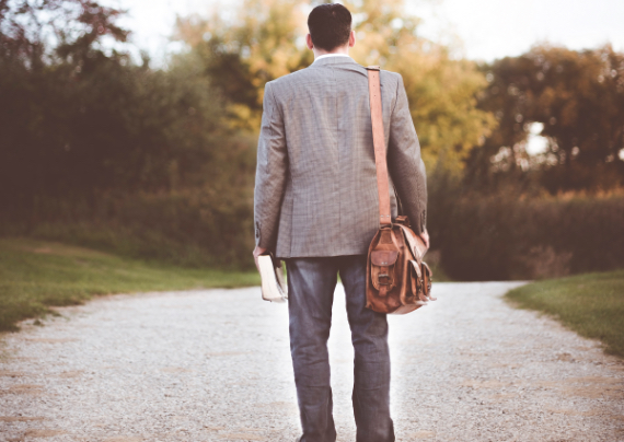 Uomo cammina con borsa alle spalle e Bibbia in mano