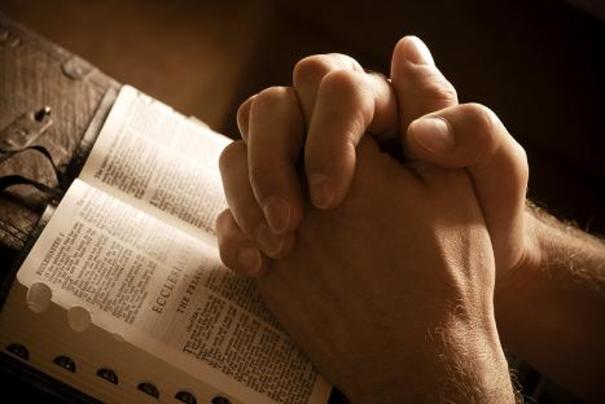 Mani giunte in preghiera su bibbia aperta