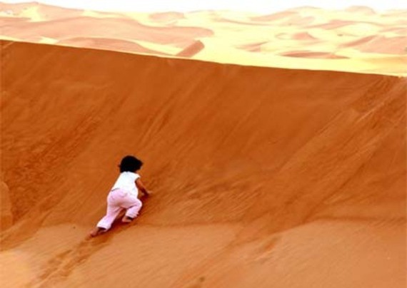 bambino si arrampica su una duna di sabbia 